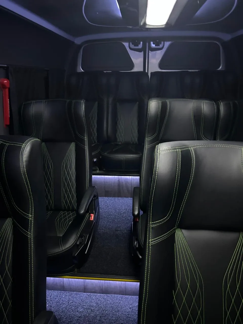 Poltronas de couro preto com costura verde e iluminação no piso